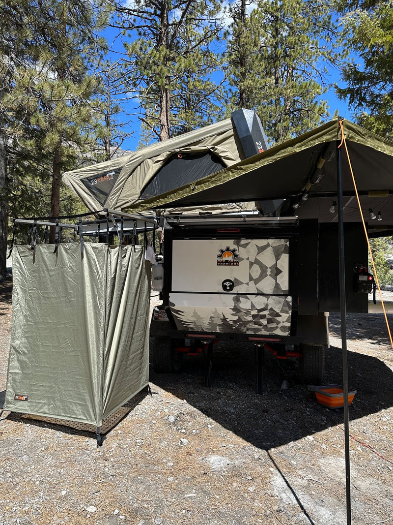 An olive green off-road camping trailer is set up with a rooftop tent, side awning, and privacy tent, perfect for an RV rental. — photo 16