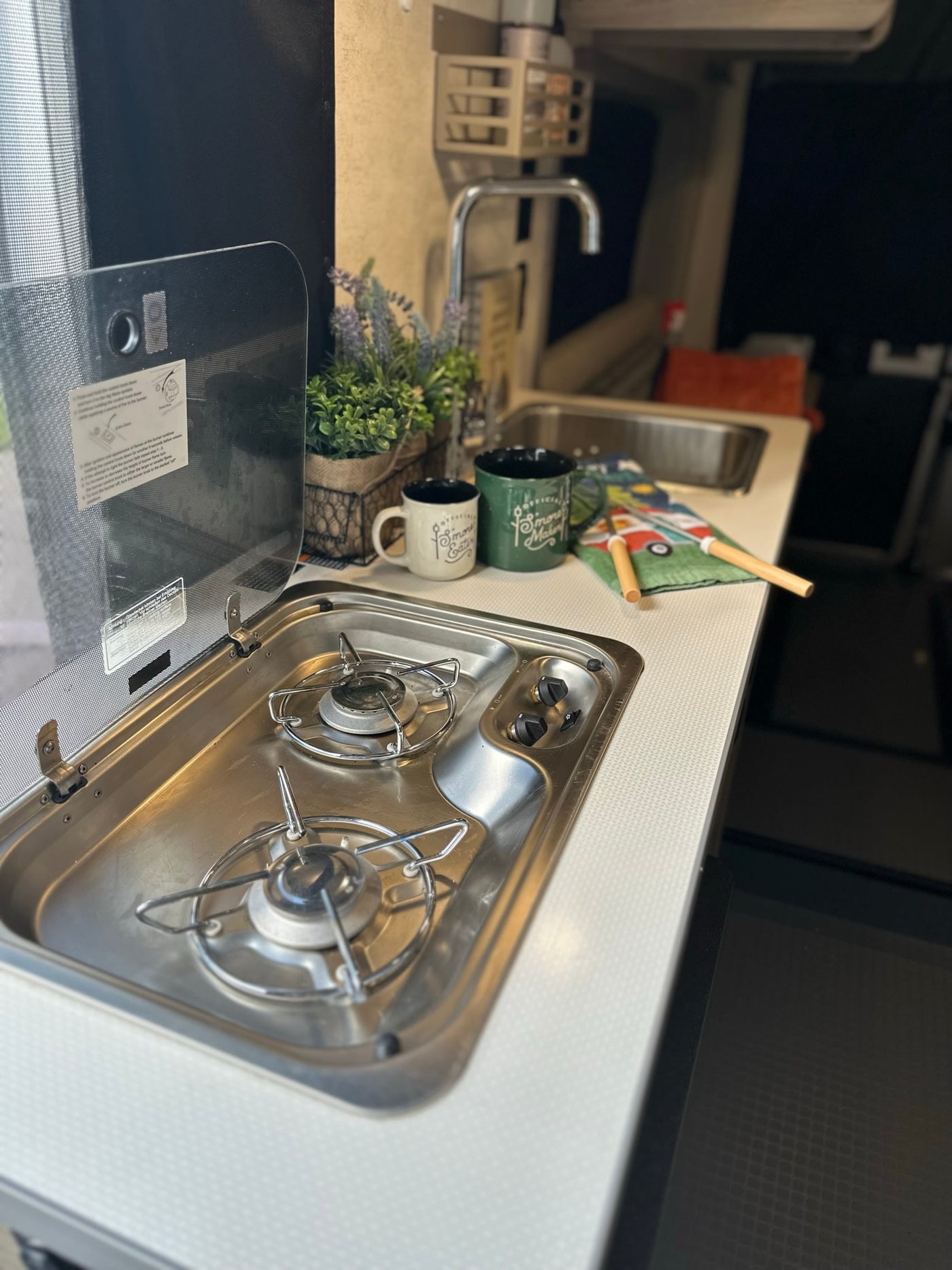 Compact RV rental kitchen featuring a two-burner stove, sink, and countertop with accessories. Ideal for cooking on the road. — photo 10