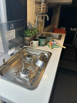 Compact RV rental kitchen featuring a two-burner stove, sink, and countertop with accessories. Ideal for cooking on the road.