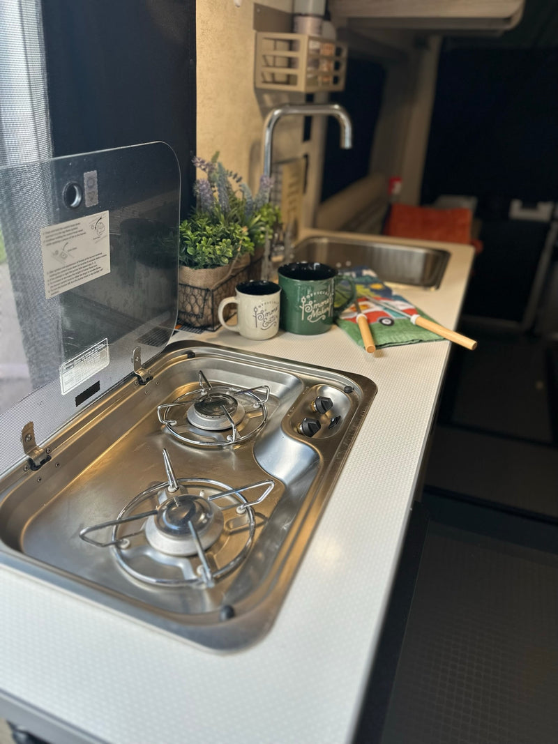 Compact RV rental kitchen featuring a two-burner stove, sink, and countertop with accessories. Ideal for cooking on the road. — photo 10