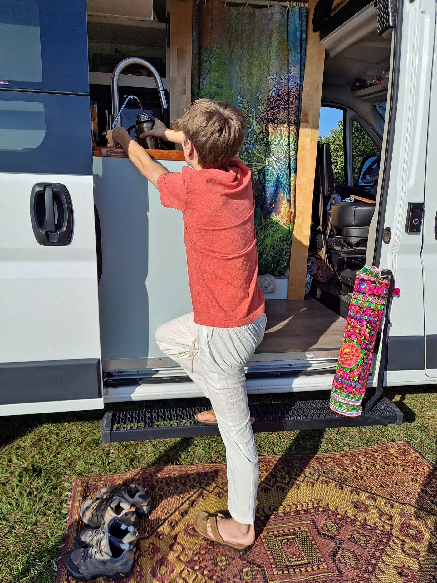 A person prepares a drink inside a white camper van, likely an RV rental. An outdoor mat and shoes sit outside the opened door. — photo 18