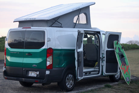 White & green Ford Transit rv rental camper van, pop-top raised, with open side doors & surfboard.