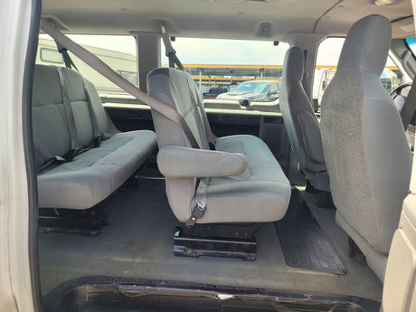 Interior view of a passenger van for RV rental, showing grey multi-row seating with seatbelts.