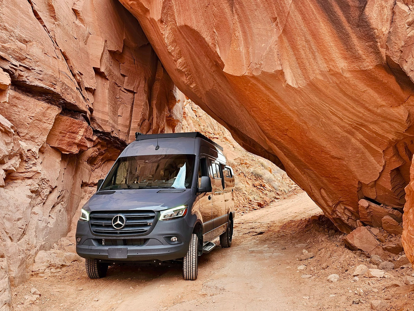 This grey camper van, perfect for rv rental adventures, navigates a rugged dirt path through a dramatic red rock canyon. — photo 5