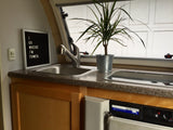 This RV rental kitchenette features a sink, plant, and a "I GO WHERE I'M TOWED" sign. Includes a Norcold fridge.