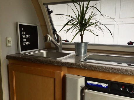 This RV rental kitchenette features a sink, plant, and a "I GO WHERE I'M TOWED" sign. Includes a Norcold fridge.