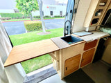Inside this RV rental, a compact kitchen with sink and extendable counter opens to an outdoor view, perfect for mobile adventures.