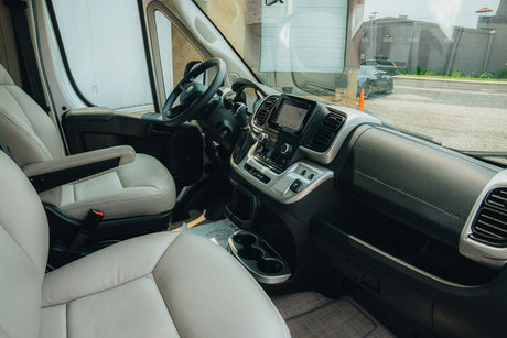RV rental's spacious van interior: comfy driver & passenger seats, modern dashboard, and outside road view.