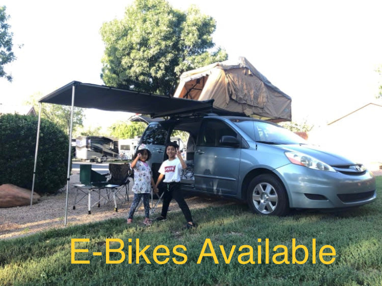 Minivan RV rental with rooftop tent and awning setup for camping. Two kids pose outside, E-Bikes Available.