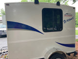 Side view of a white Rouser Runaway RV rental, with blue stripes, a window, and a front-mounted spare tire.