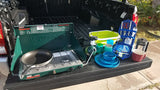Setup for an RV rental adventure: Coleman stove, pan, dishes, and kitchen tools displayed on a truck tailgate.