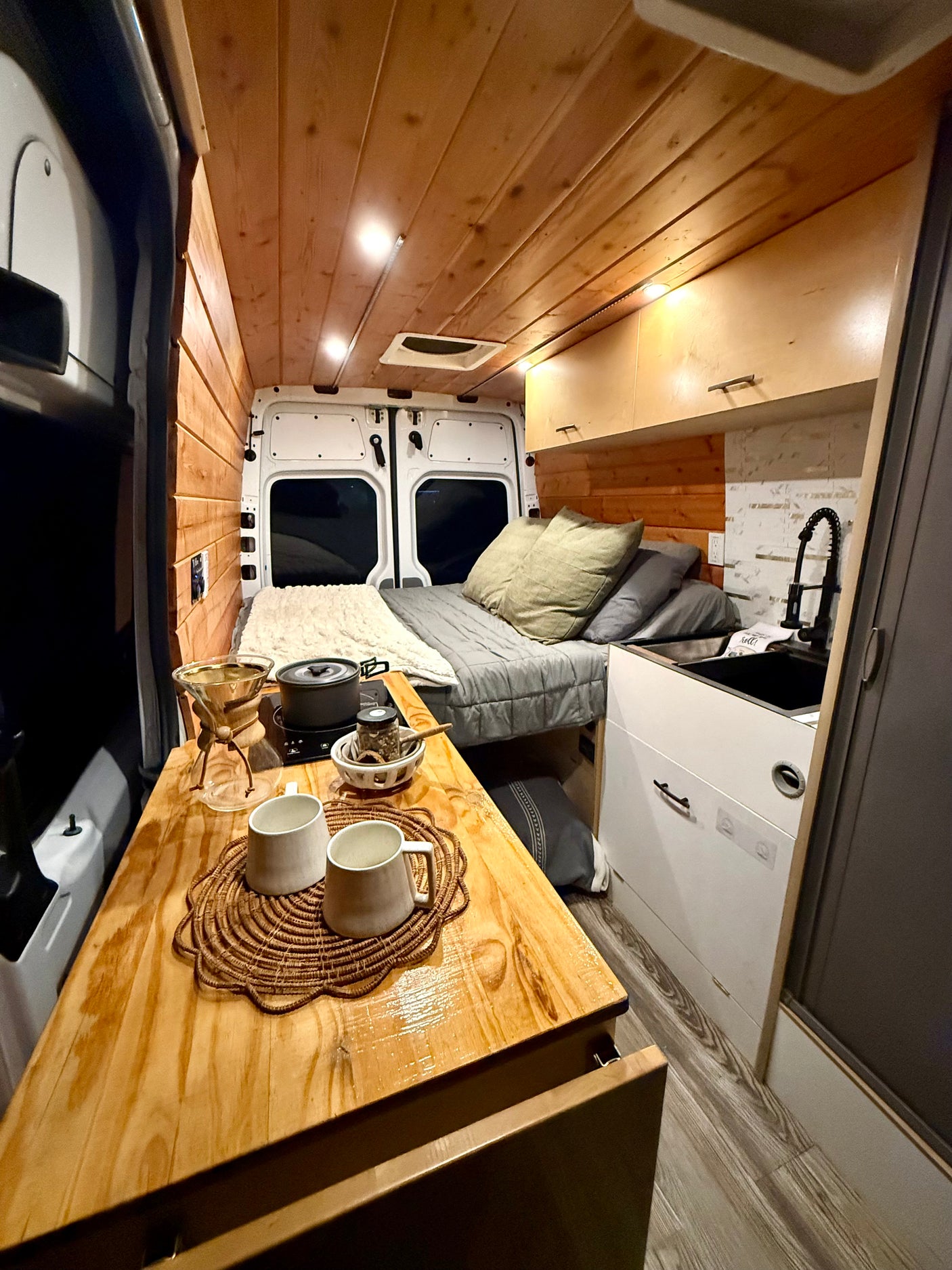 Cozy RV rental interior with wooden walls & ceiling, bed, kitchenette, and coffee station. Perfect for travel!