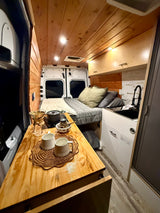 Cozy RV rental interior with wooden walls & ceiling, bed, kitchenette, and coffee station. Perfect for travel!