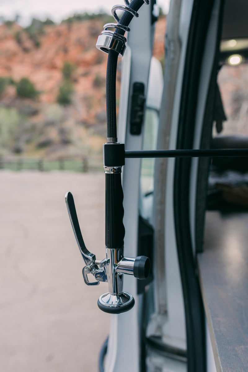 Close-up of a chrome outdoor spray head with a black hose on an RV rental van, with a natural landscape background. — photo 9