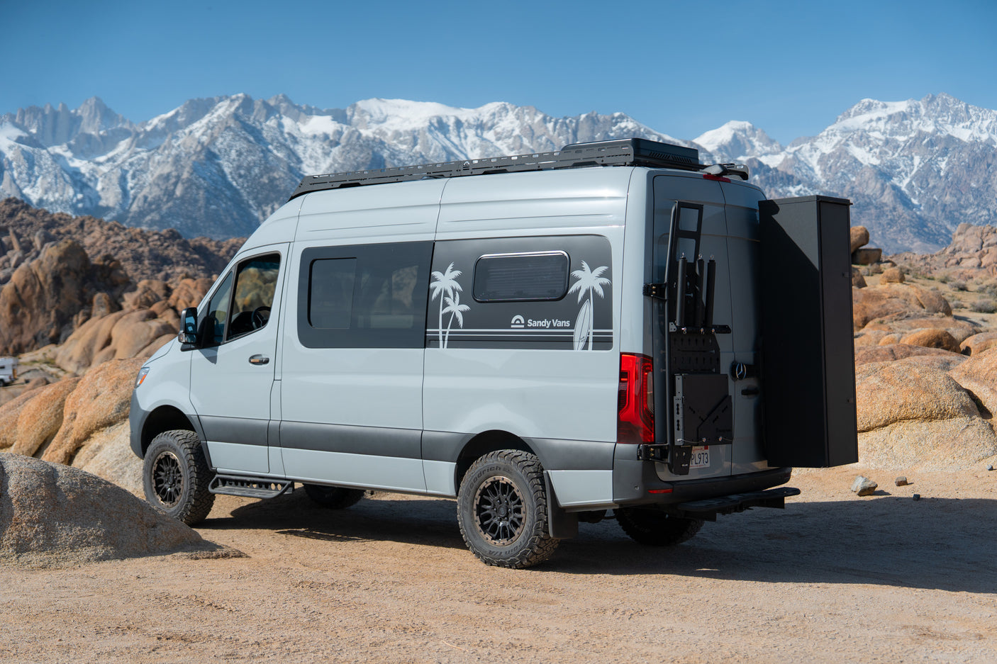 This custom Sandy Vans Sprinter rv rental is adventure-ready, parked off-road with stunning snow-capped mountains in the background.