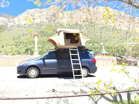 Minivan with a rooftop tent set up for camping, offering an RV rental experience in the mountains. Perfect for outdoor adventures.