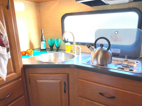 This rv rental features a well-equipped compact kitchen with a sink, stove, and kettle, ready for your road trip meals.