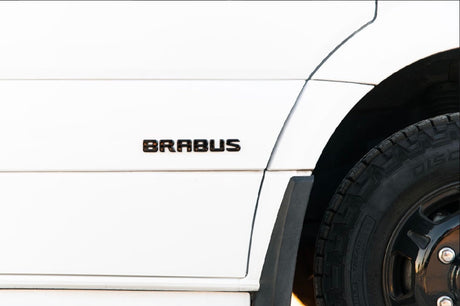 White custom RV rental side view, featuring a BRABUS emblem and all-terrain tire.