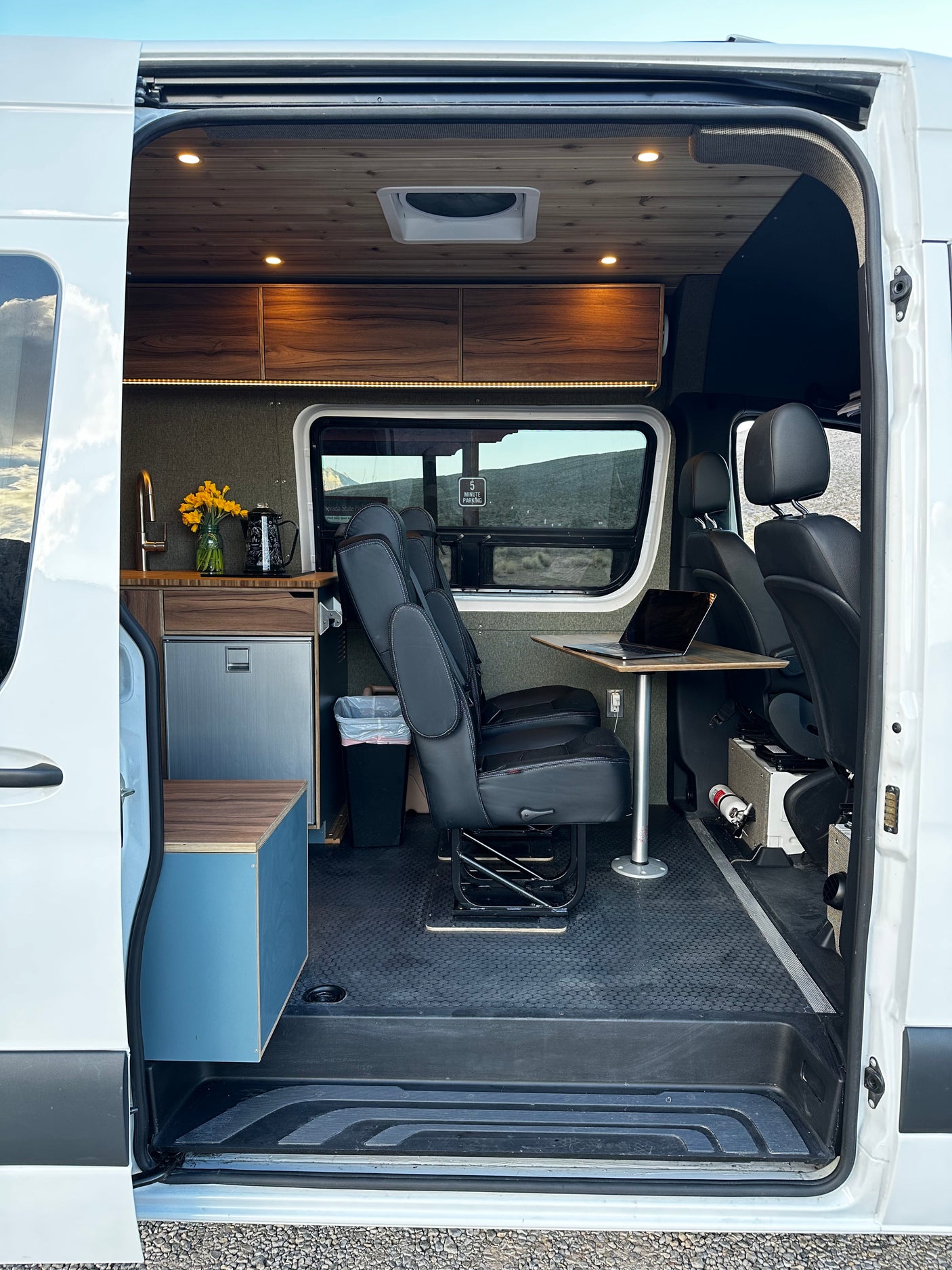 Discover this stylish rv rental van conversion interior, featuring a kitchen, swivel chairs, and a comfortable workspace.