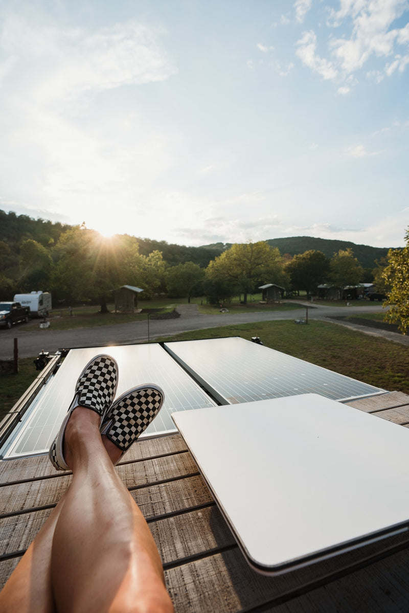 Relaxing from an RV rental, feet in checkered shoes propped on a deck, with solar panels and a sunny campground view. — photo 8