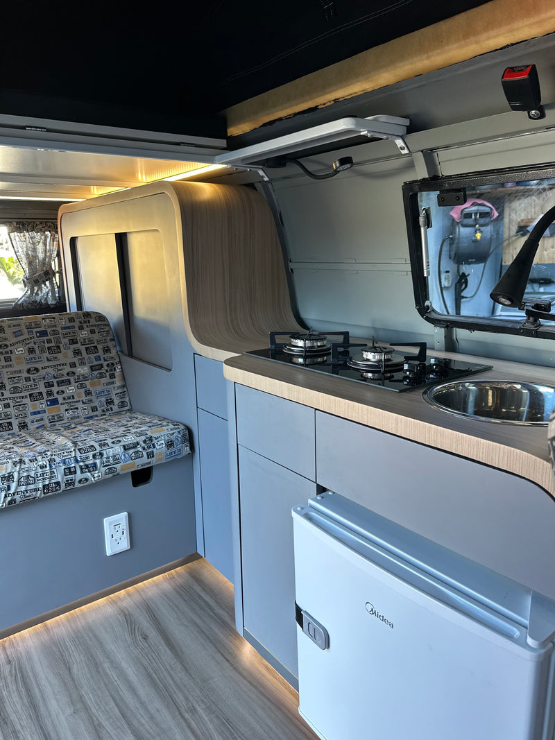 Clean RV rental interior with a kitchenette (stove, sink), seating area, mini-fridge, and illuminated wood flooring. — photo 6