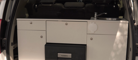 This RV rental features a compact campervan kitchen setup with a sink, Dometic fridge, and storage cabinets for comfortable travel.