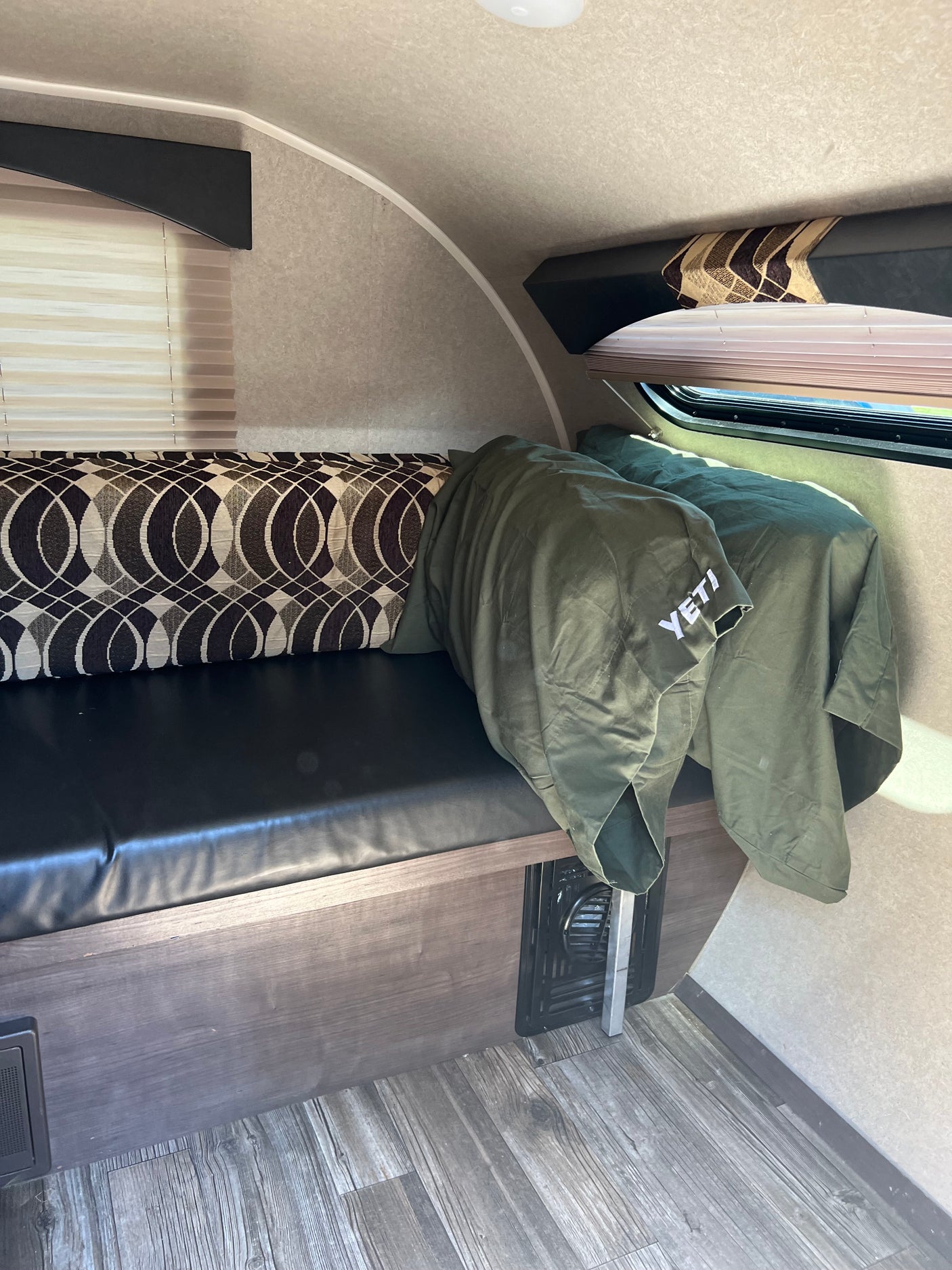 Interior of an RV rental showing a comfy bench seat with patterned cushions, a green YETI blanket, and window.