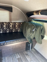 Interior of an RV rental showing a comfy bench seat with patterned cushions, a green YETI blanket, and window.