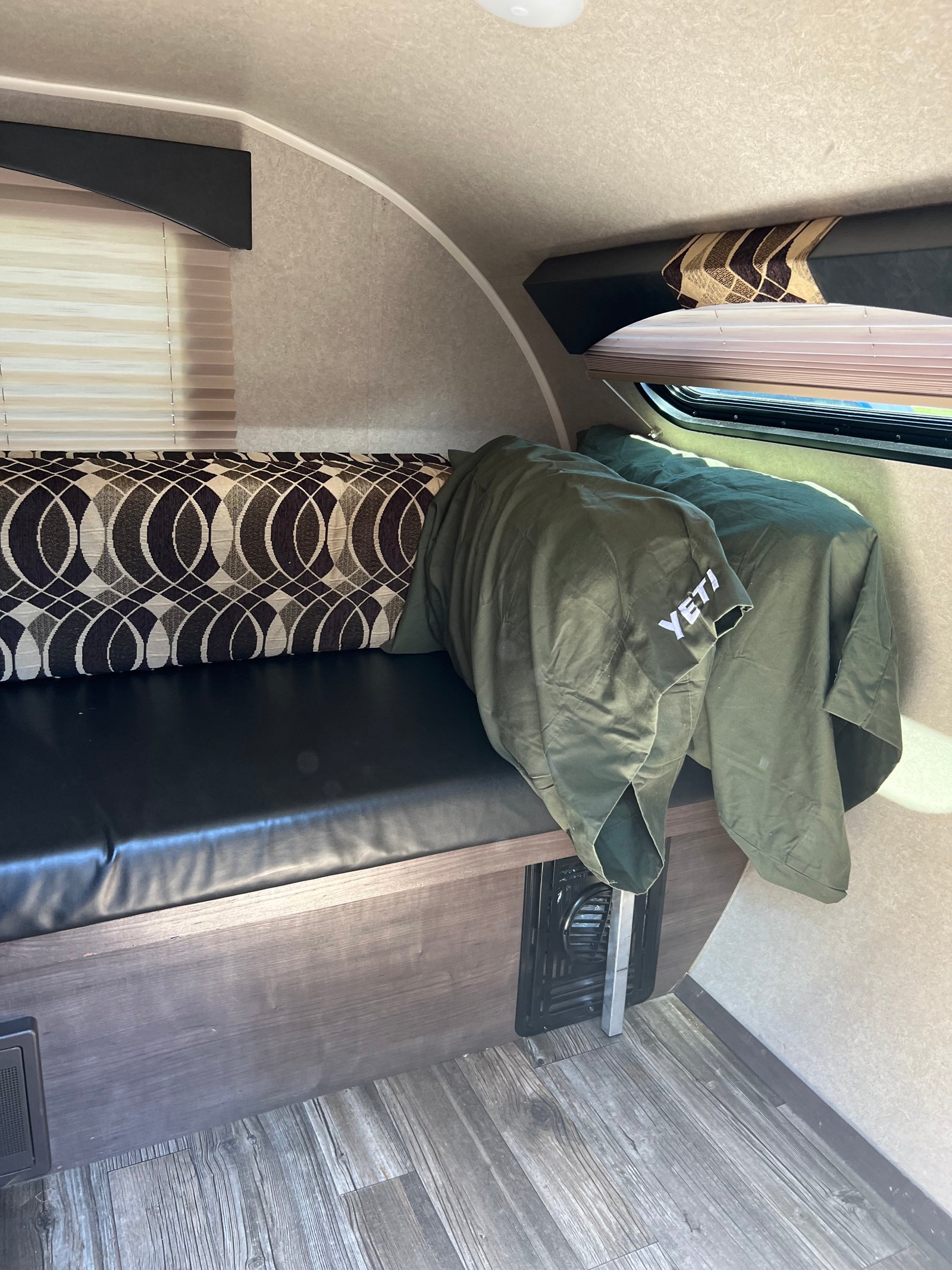 Interior of an RV rental showing a comfy bench seat with patterned cushions, a green YETI blanket, and window.