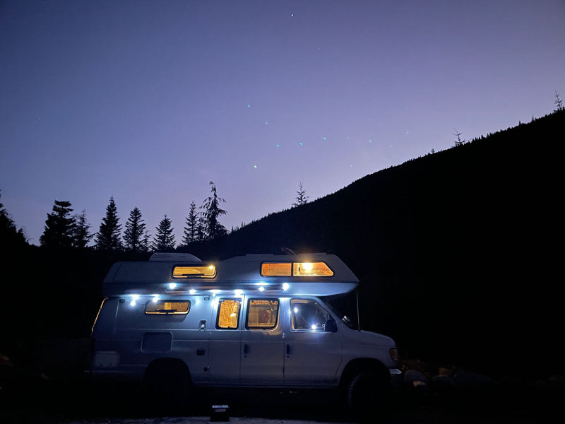  parked on a dirt road surrounded by misty mountains and tall trees. Perfect for your next **RV rental** adventure.|A white RV rental glows warmly at night — photo 2