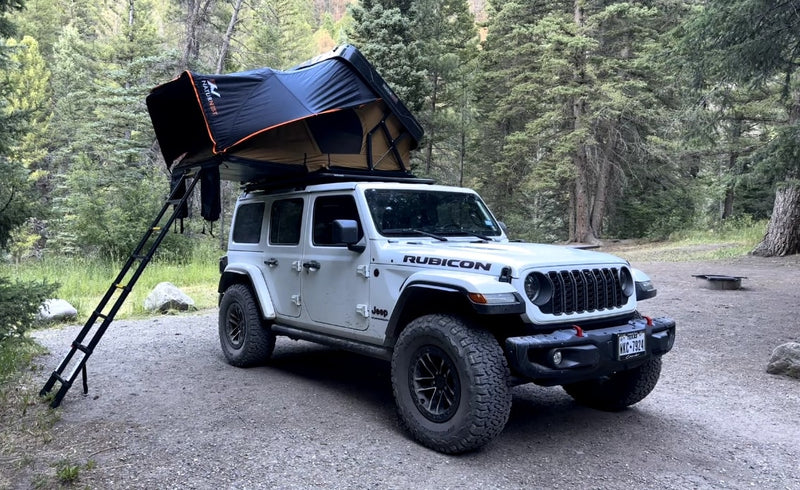  ready for off-road camping. An adventurous rv rental option in the forest.|White Jeep Wrangler with a rooftop tent set up in a forest. Experience outdoor camping with this unique RV rental.|White Jeep Wrangler Rubicon 4x4 with a rooftop tent. An ideal RV rental for rugged camping and outdoor adventure.|Experience adventure with this white Jeep Rubicon featuring a rooftop tent — photo 2