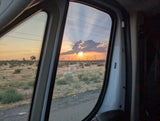 An RV rental window frames a stunning desert sunset, showing Joshua trees & distant power lines. Scenic road trip view.