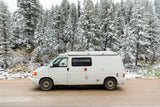 White camper van RV rental in a snowy pine forest. Ideal for exploring winter landscapes.