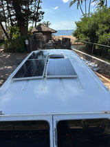RV rental van with rooftop solar panels, offering off-grid power by a sunny tropical beach and ocean views.