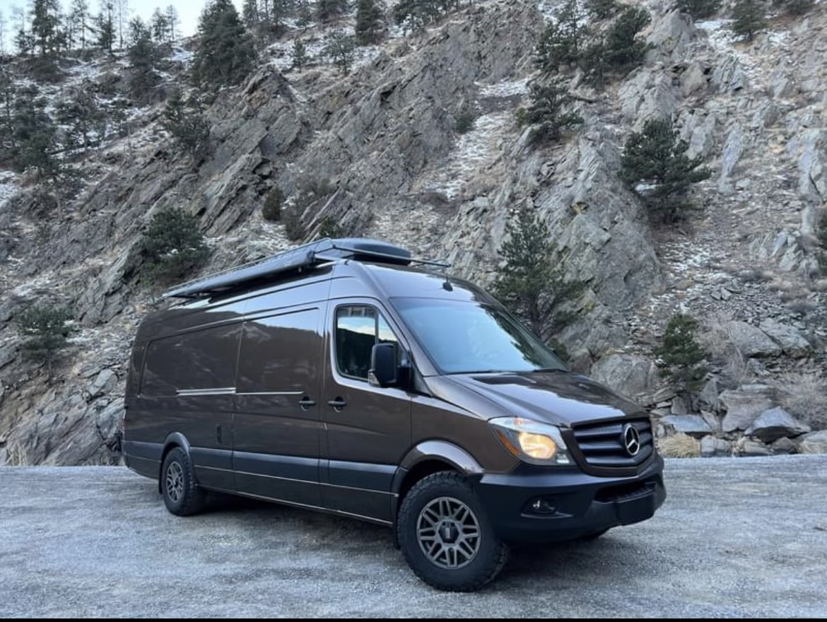  parked on a snowy road.|Dark brown Mercedes Sprinter adventure van