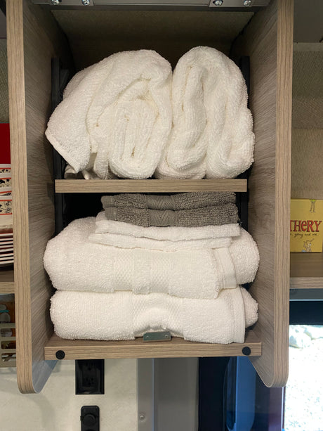 Clean, folded towels neatly stacked in an RV rental's wooden cabinet. White and gray towels are organized on three shelves.