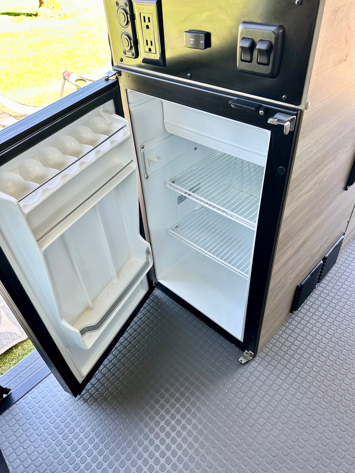 **RV rental** interior features: open, empty mini-fridge with egg holder, control panel (AC/DC/USB outlets, "Coach Batt" switch). — photo 8