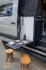 RV rental outdoor dining setup: campervan with a side table, wine, glasses, plates, and stools. Ready for adventure.