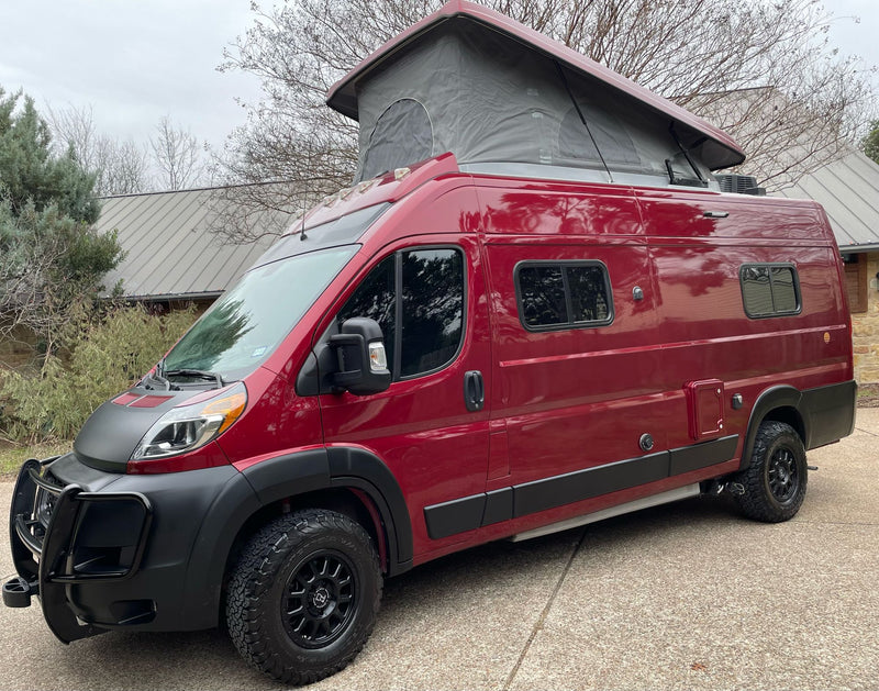 This bright red pop-top RV rental features off-road tires and a front bull bar for adventure.|Striking red rv rental camper van with pop-top extended. Open side door reveals custom interior. Equipped for adventure with off-road tires.|This eye-catching red pop-top camper van — photo 1
