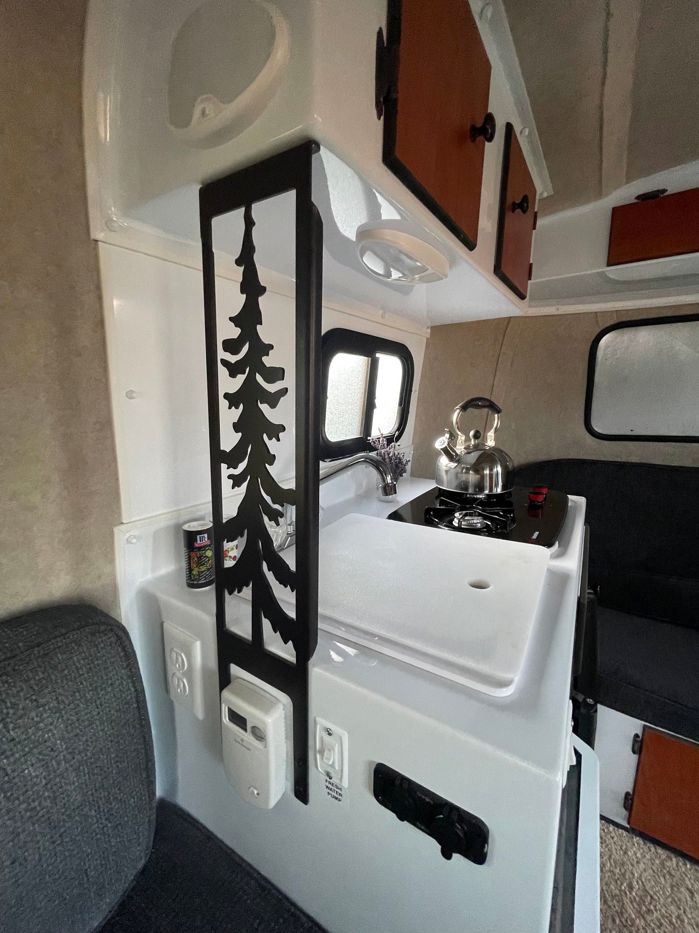 This RV rental features a compact kitchen with a sink, stovetop, wood cabinets, and a unique metal tree partition.