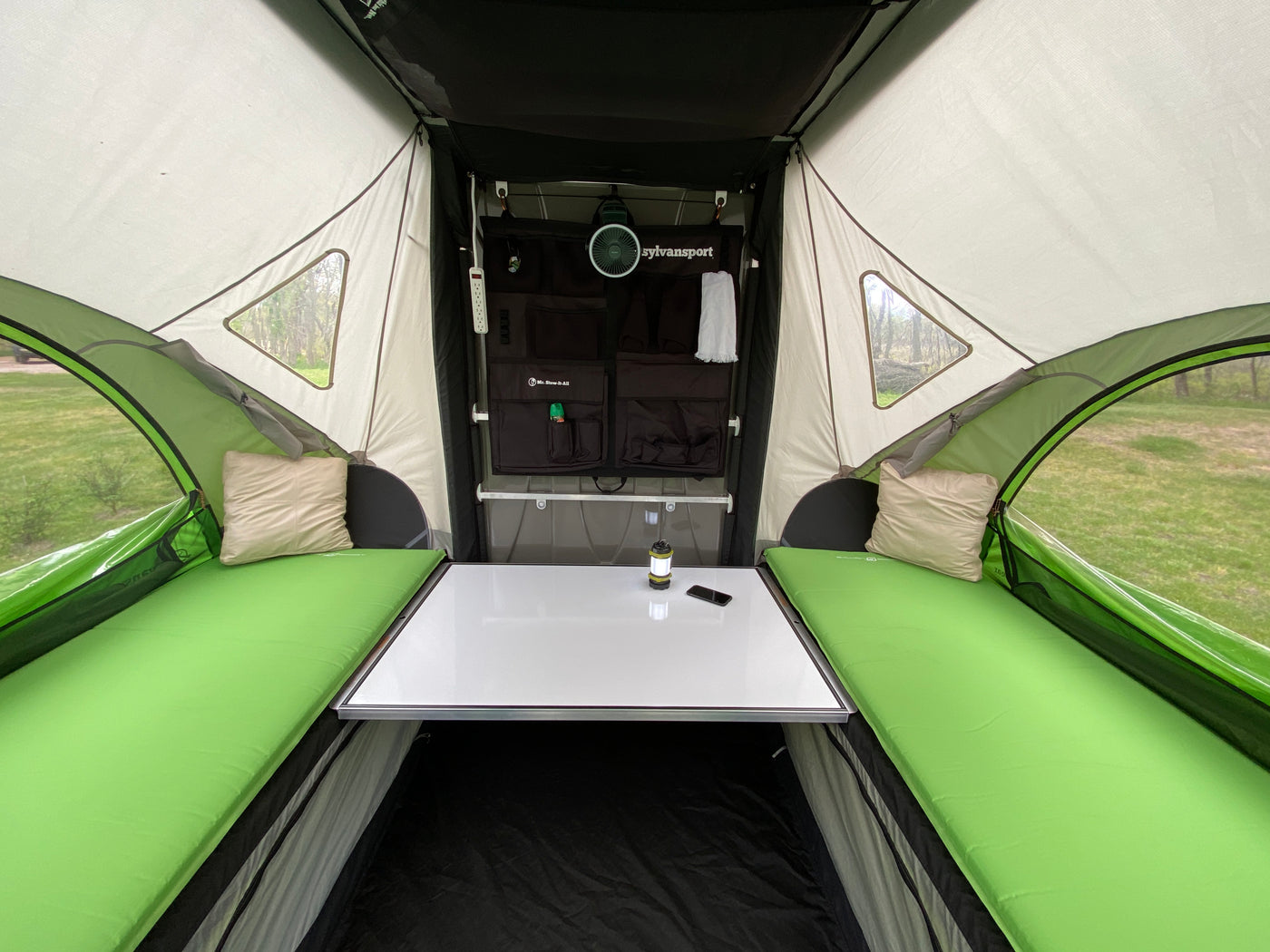 Cozy SylvanSport RV rental interior: green beds, central table, and storage for comfortable camping or outdoor travel. — photo 15