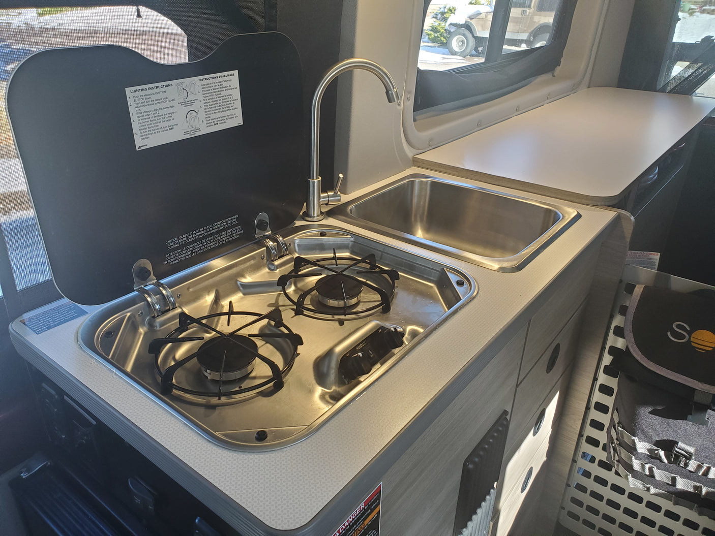 Compact kitchen setup in an RV rental, featuring a two-burner stove, a sink with faucet, and countertop space.