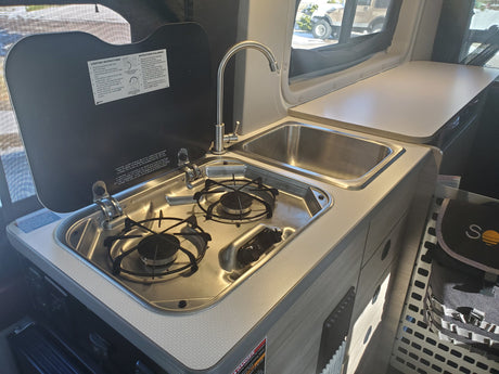 Compact kitchen setup in an RV rental, featuring a two-burner stove, a sink with faucet, and countertop space.