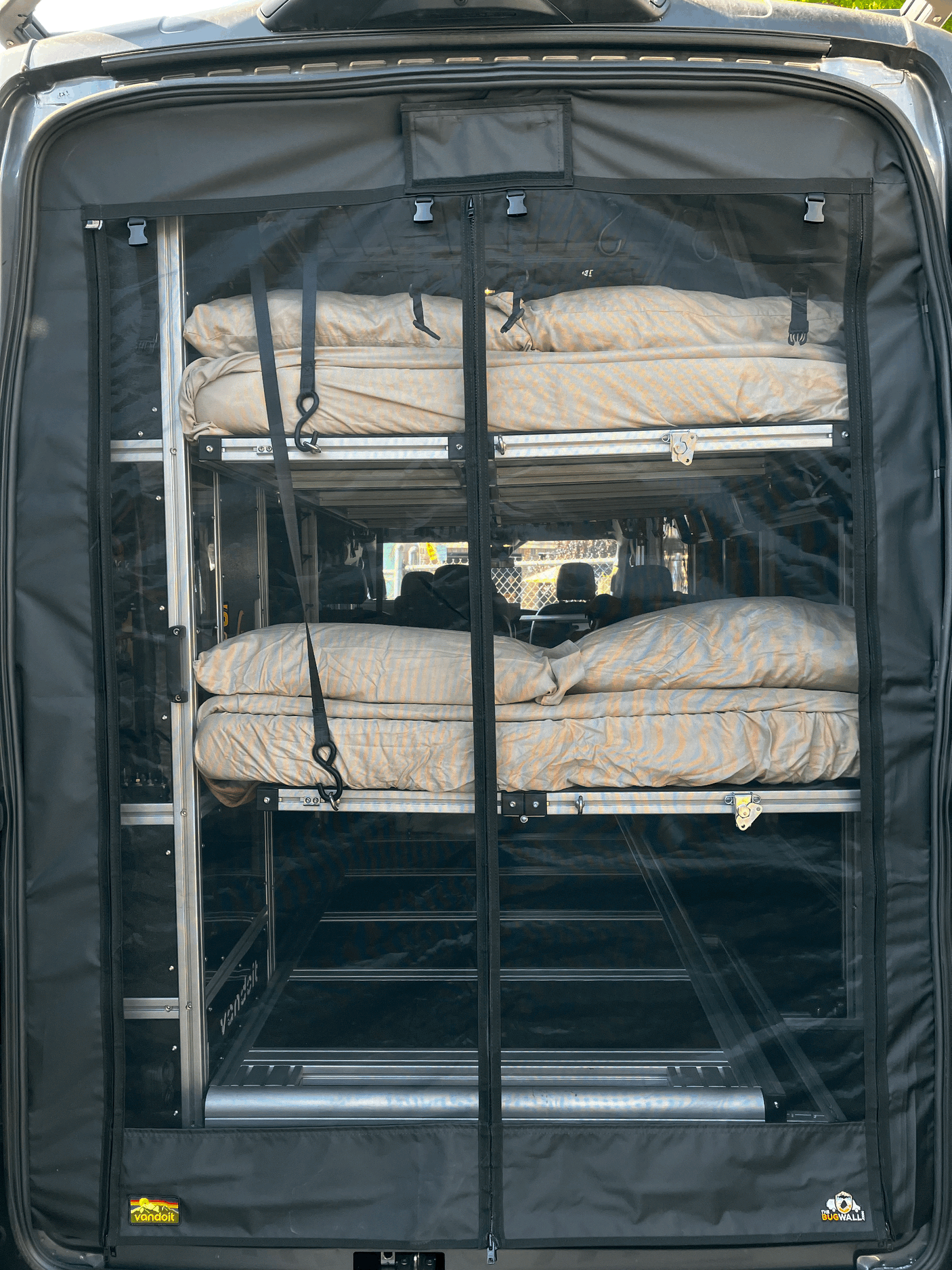 RV rental: Rear view of a van's modular bunk bed system with bedding, visible through a clear divider for versatile camping.