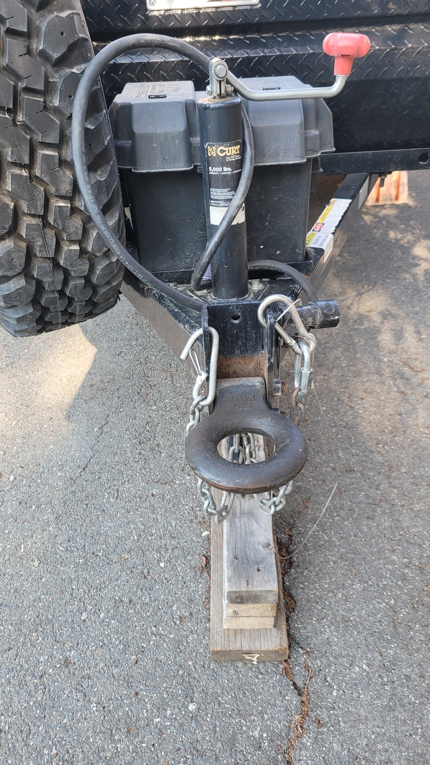 Hitching system of an RV rental trailer showing the heavy-duty pintle hitch, CURT jack, spare tire, and safety chains.