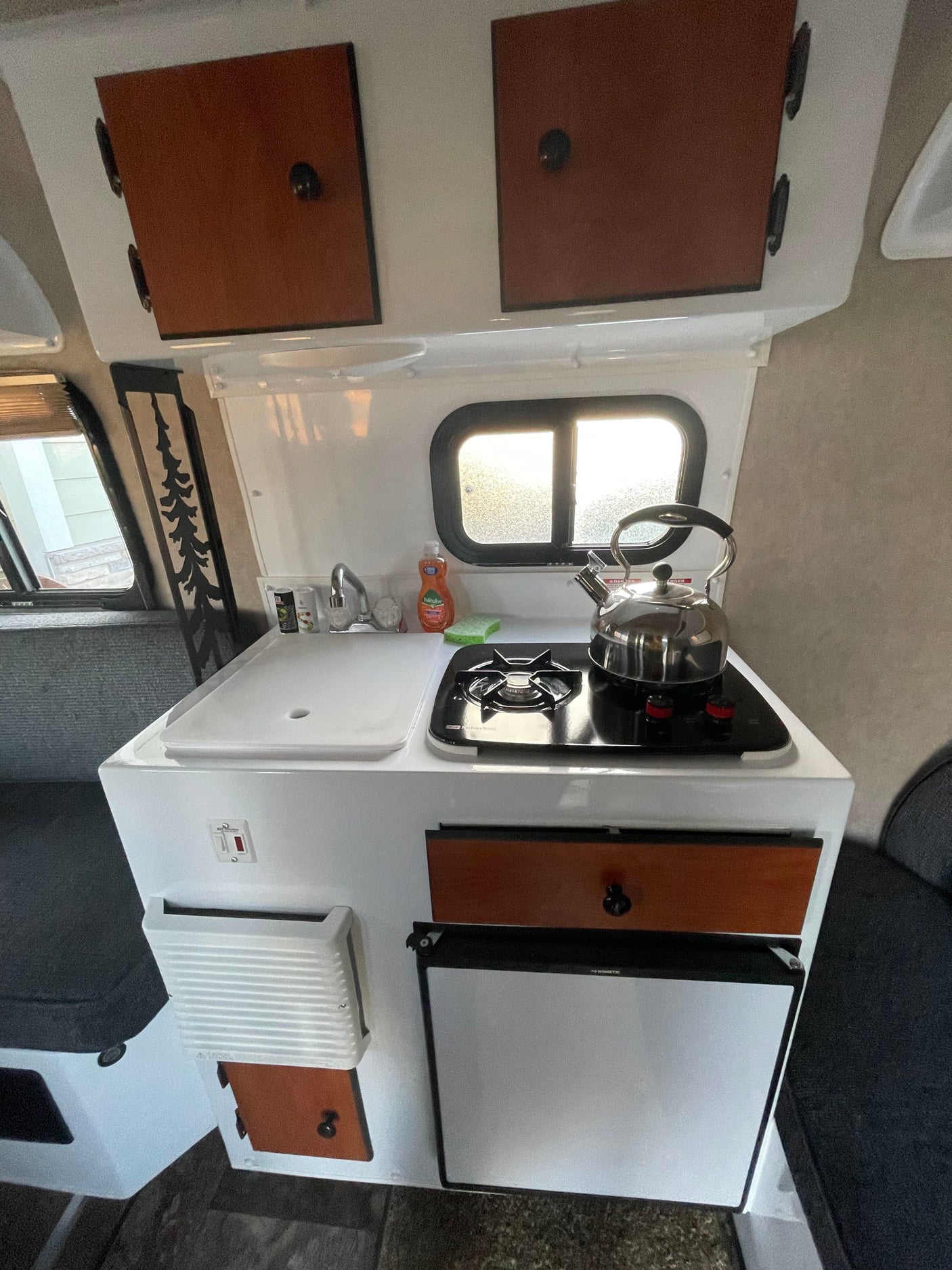 Compact RV kitchen in this rental: sink, stove, kettle, fridge, and wood cabinets. An efficient cooking space.