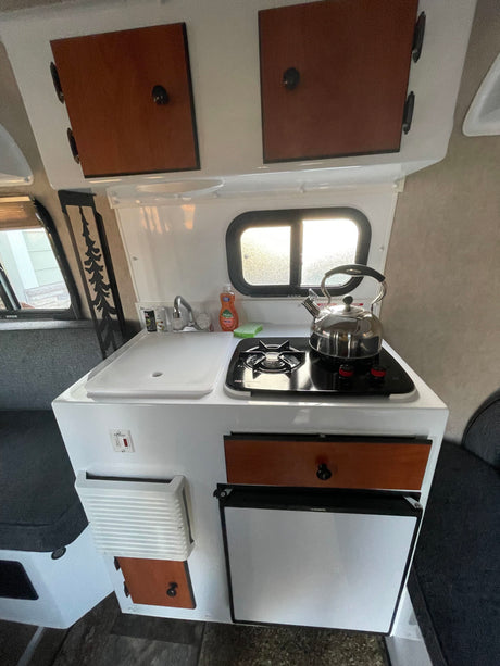 Compact RV kitchen in this rental: sink, stove, kettle, fridge, and wood cabinets. An efficient cooking space.