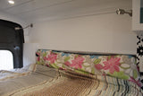 Inside an RV rental: a cozy bed with striped comforter, floral pillow, and two wall-mounted reading lights.