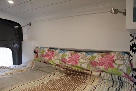Inside an RV rental: a cozy bed with striped comforter, floral pillow, and two wall-mounted reading lights.