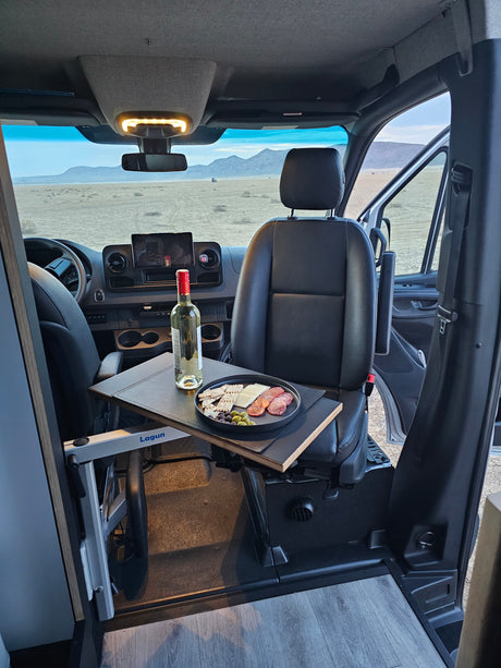 Inside a comfy RV rental: charcuterie plate & wine on a table, with scenic desert mountains visible through the windshield.